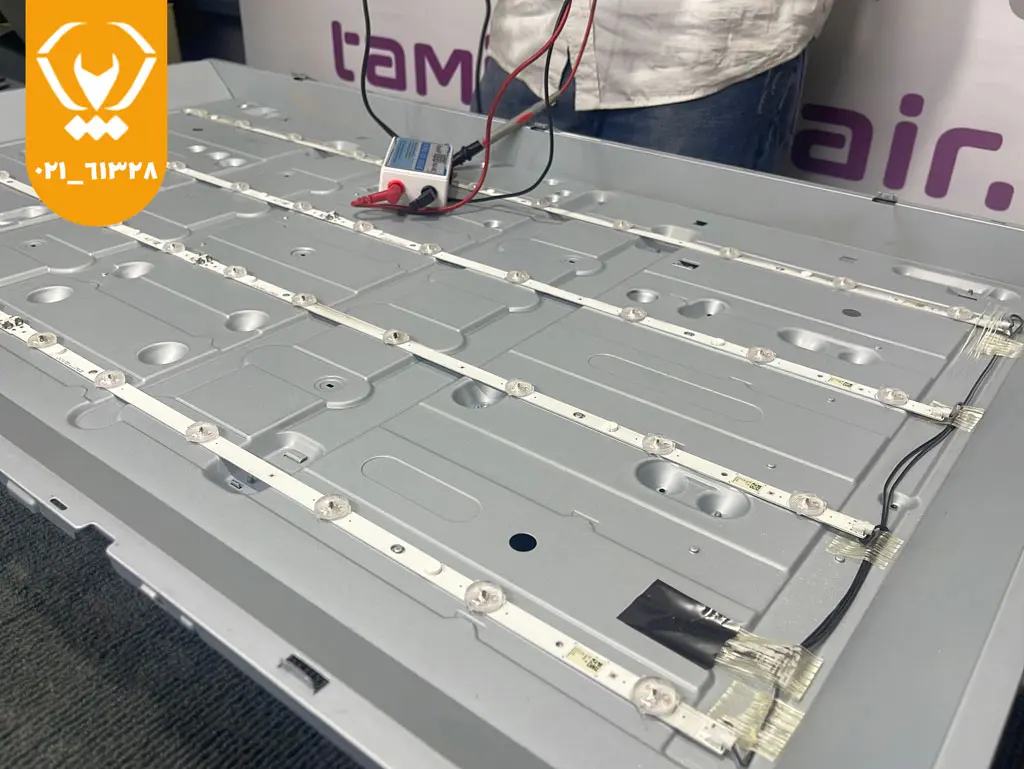 تکنسین در حال بررسی و خشککردن برد داخلی تلویزیون الجی پس از نفوذ آب به منظور تعمیر آبخوردگی